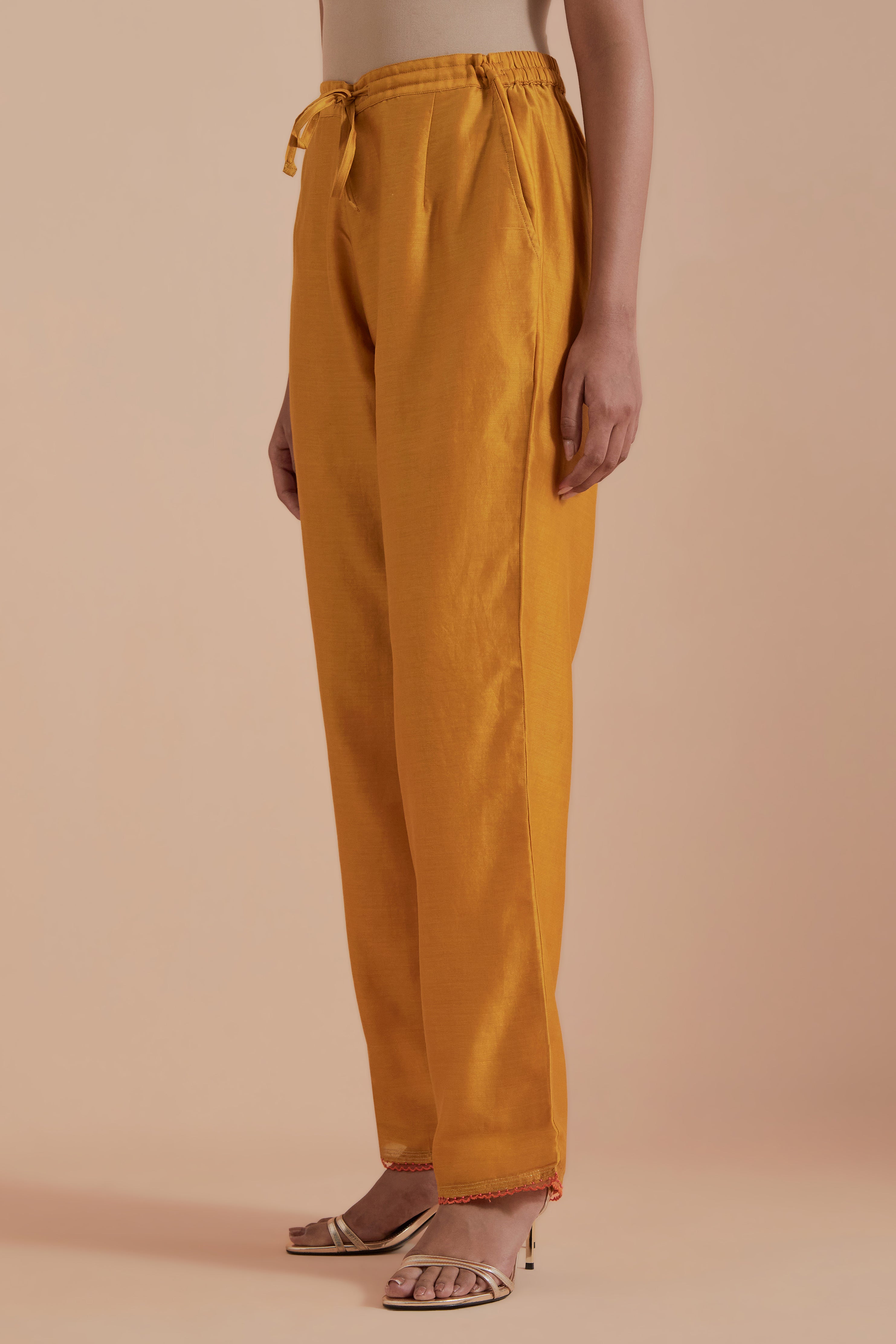 Mustard silk chanderi straight pants detailed with scalloped organza edging at the hem, delicately highlighted with gold zari quilting.