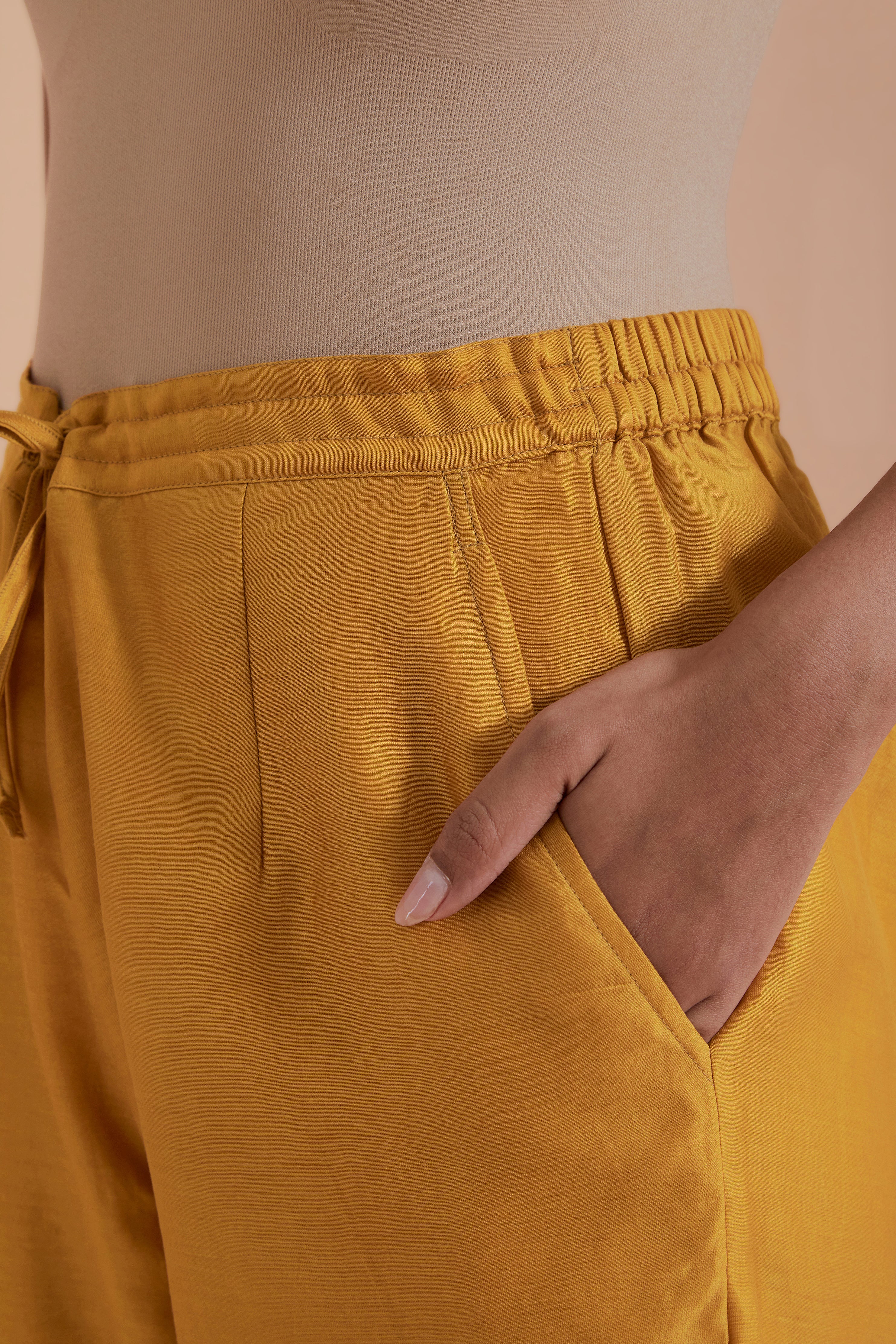 Mustard silk chanderi straight pants detailed with scalloped organza edging at the hem, delicately highlighted with gold zari quilting.
