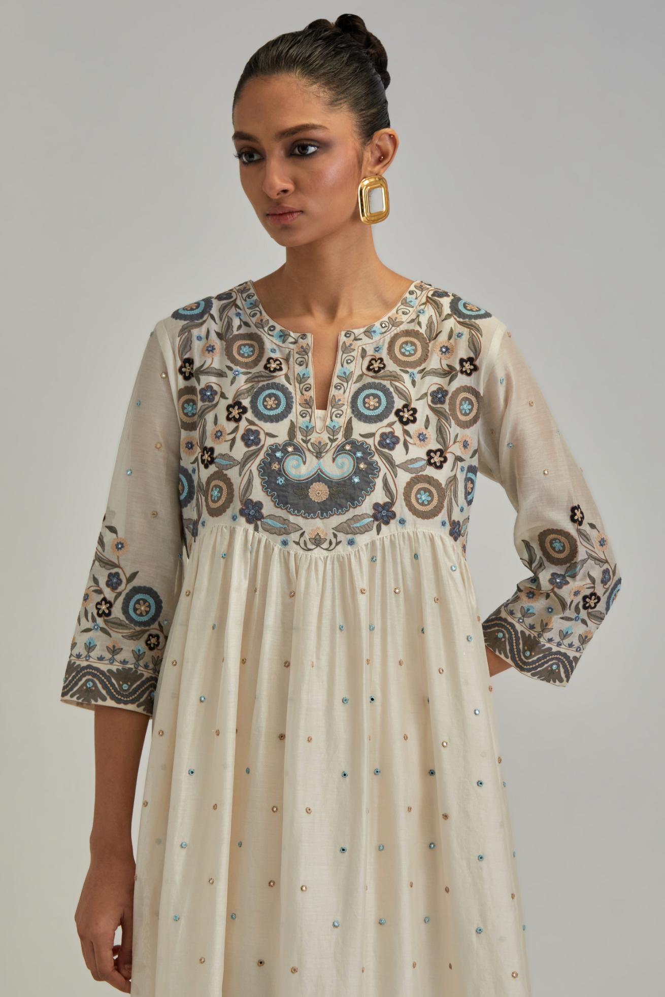 Off White silk Chanderi kurta-dress set with a wavy high-waist and fine gathers. The yoke is fully embroidered with earthy coloured circular appliqué and Aari thread work.