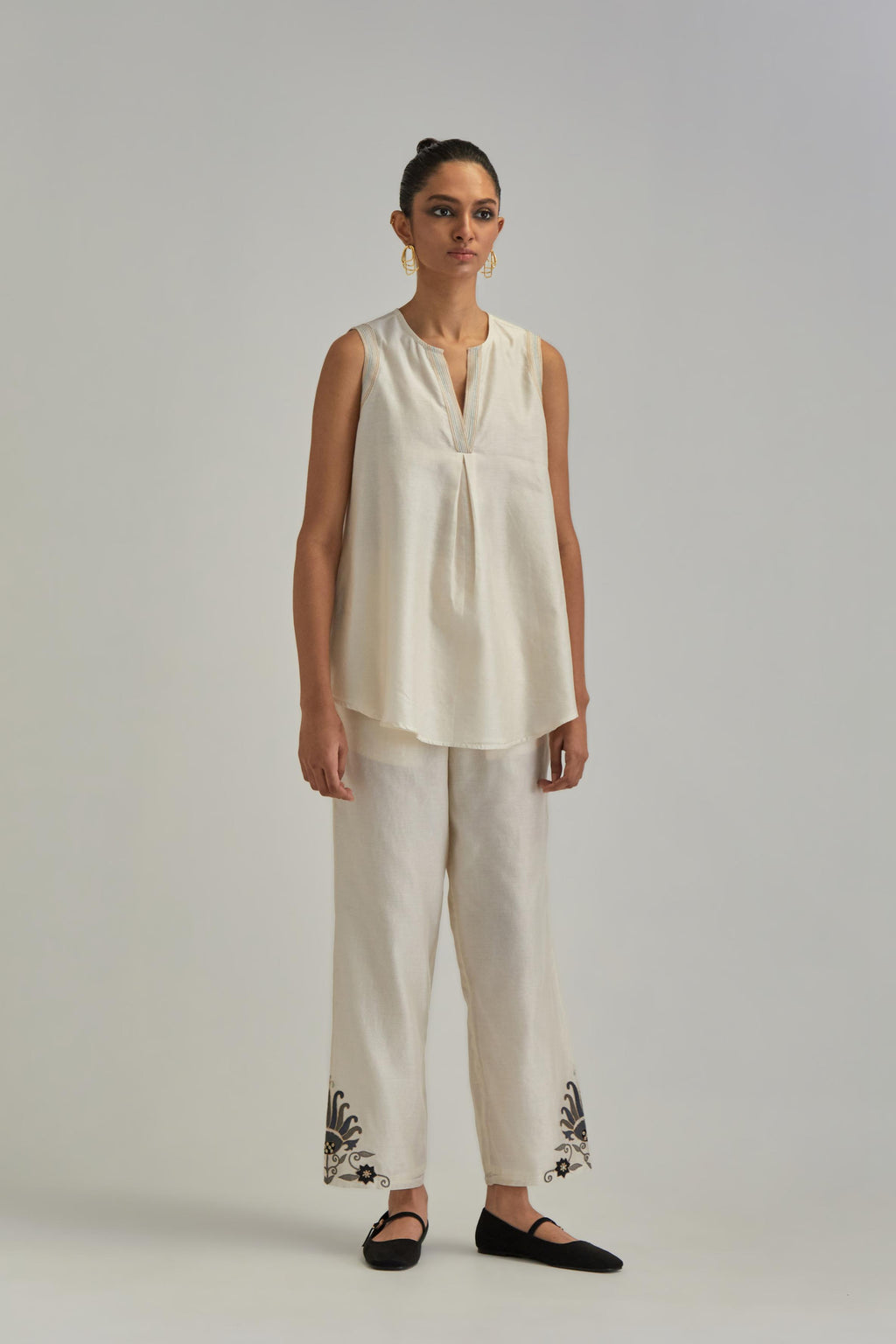 Off White short front open A-line jacket, fully embroidered with bold appliqué flowers, earthy-coloured Aari thread work and silk tassels, paired with Off white silk Chanderi straight pants with earthy coloured appliqué at hem.