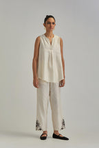 Off White short front open A-line jacket, fully embroidered with bold appliqué flowers, earthy-coloured Aari thread work and silk tassels, paired with Off white silk Chanderi straight pants with earthy coloured appliqué at hem.