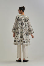 Off White short front open A-line jacket, fully embroidered with bold appliqué flowers, earthy-coloured Aari thread work and silk tassels, paired with Off white silk Chanderi straight pants with earthy coloured appliqué at hem.