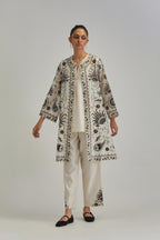 Off White short front open A-line jacket, fully embroidered with bold appliqué flowers, earthy-coloured Aari thread work and silk tassels, paired with Off white silk Chanderi straight pants with earthy coloured appliqué at hem.