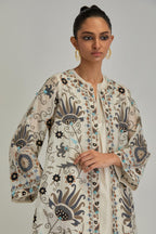 Off White short front open A-line jacket, fully embroidered with bold appliqué flowers, earthy-coloured Aari thread work and silk tassels, paired with Off white silk Chanderi straight pants with earthy coloured appliqué at hem.