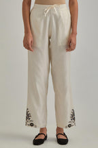 Off white silk Chanderi straight pants with earthy coloured appliqué at hem.