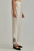 Off white silk Chanderi straight pants with earthy coloured appliqué at hem.