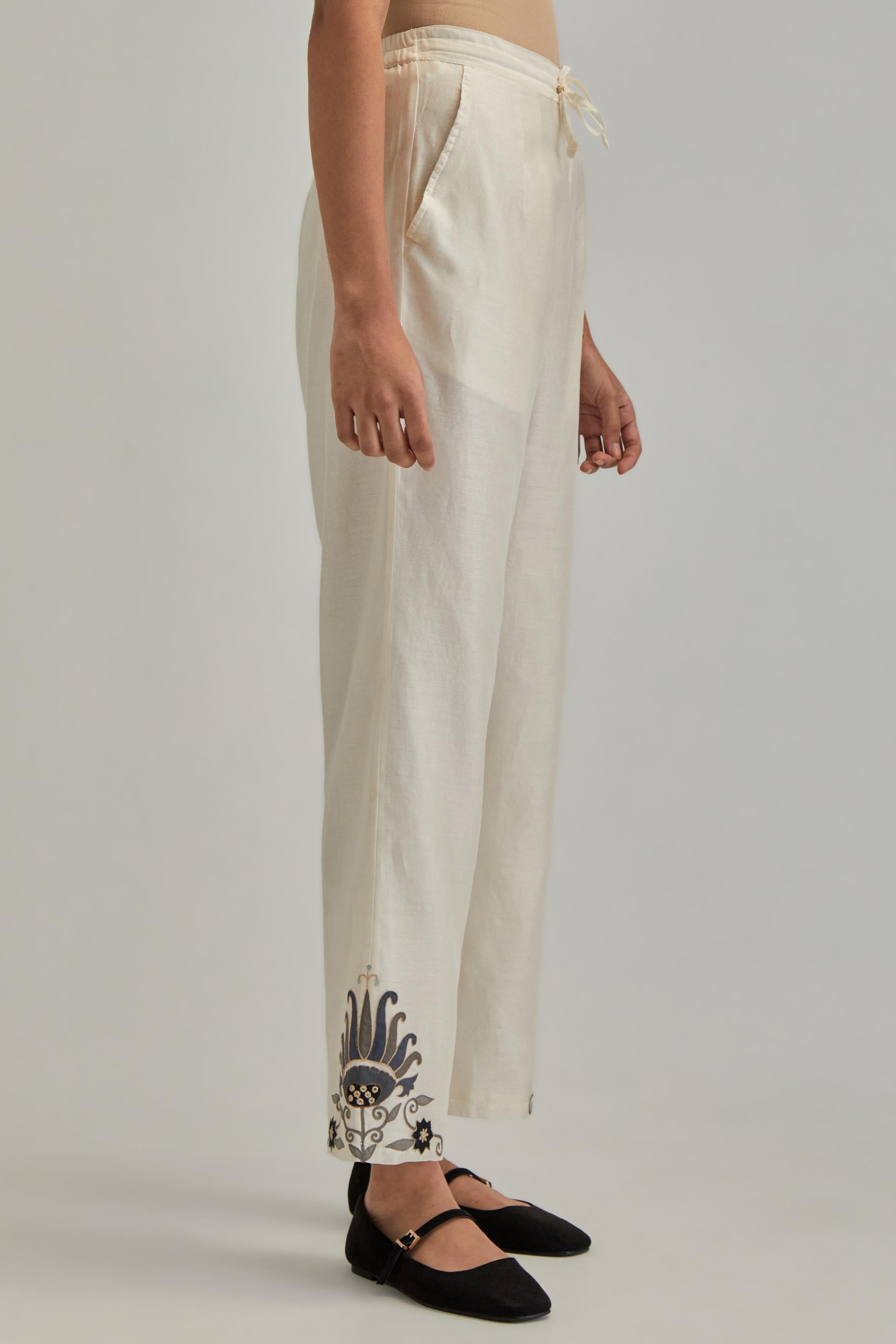 Off white silk Chanderi straight pants with earthy coloured appliqué at hem.