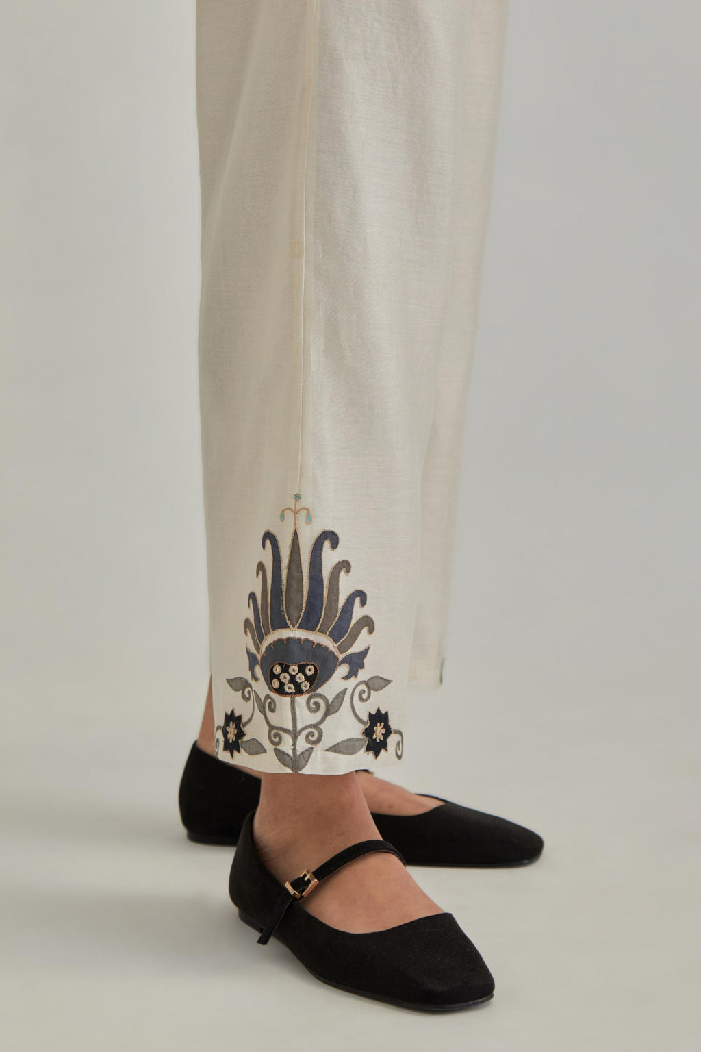 Off white silk Chanderi straight pants with earthy coloured appliqué at hem.