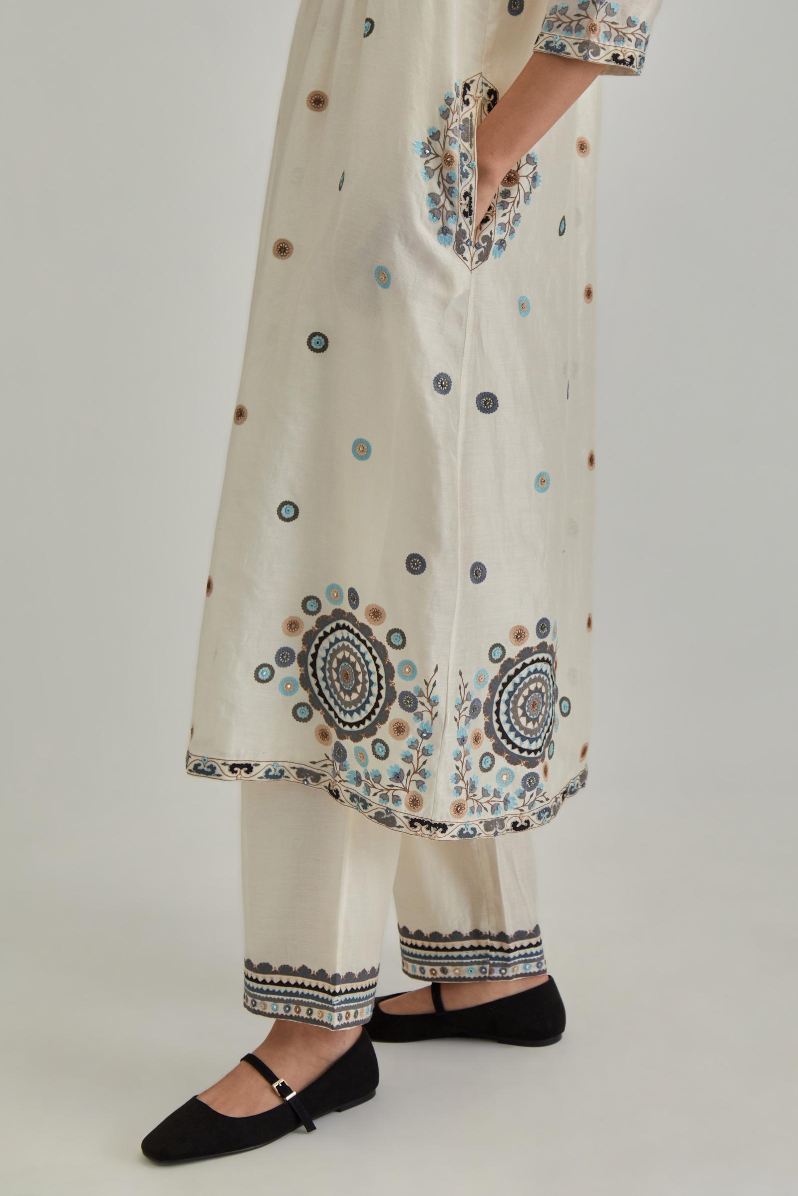 Off White silk Chanderi gathered kurta-dress set with appliqué stripes along with Aari thread work flowers and floral trellises along with a circular appliqued motif.