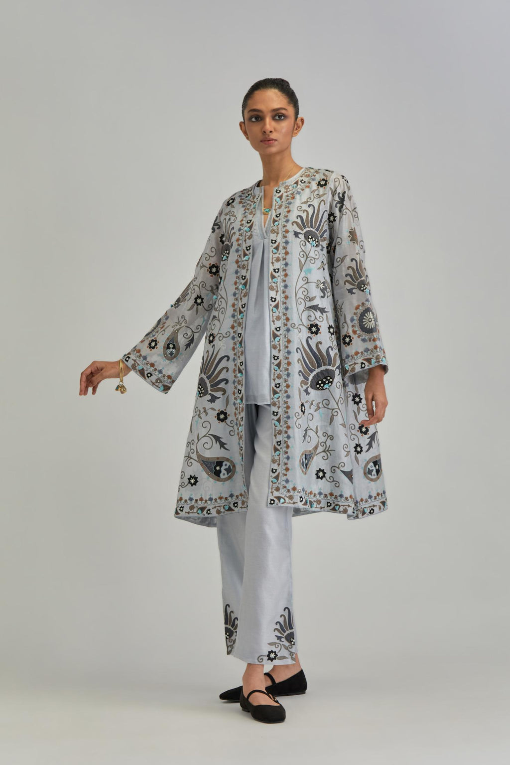 Blue short front open A-line jacket, fully embroidered with bold appliqué flowers, earthy-coloured Aari thread work and silk tassels, paired with Blue silk Chanderi straight pants with earthy coloured appliqué at hem.