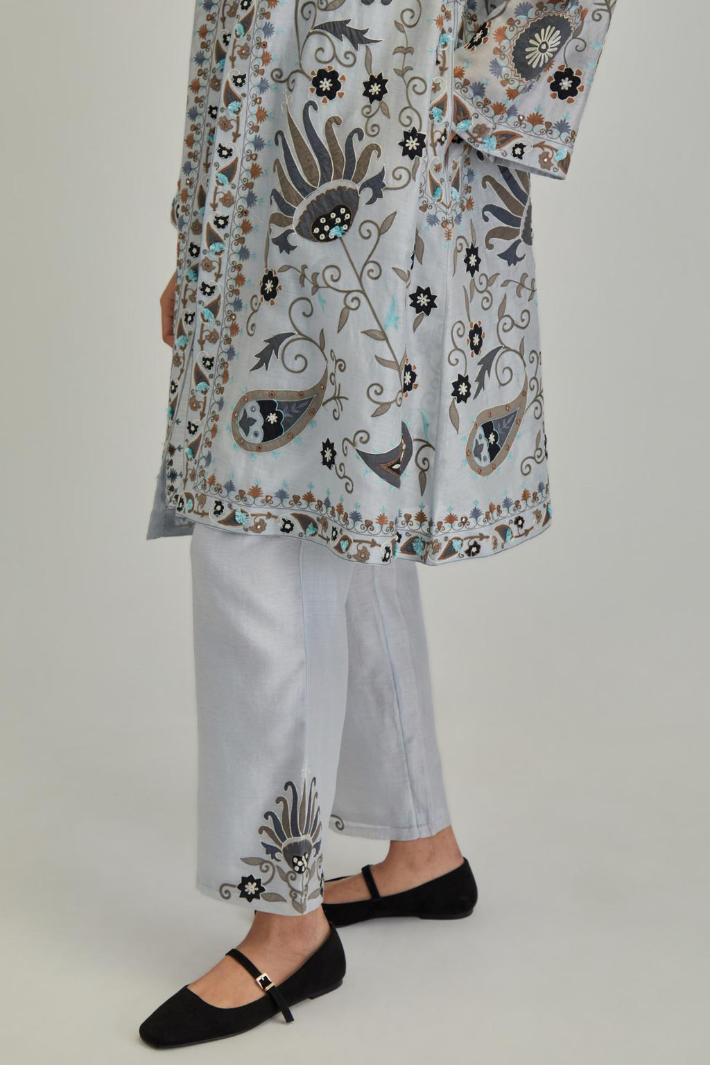 Blue short front open A-line jacket, fully embroidered with bold appliqué flowers, earthy-coloured Aari thread work and silk tassels, paired with Blue silk Chanderi straight pants with earthy coloured appliqué at hem.