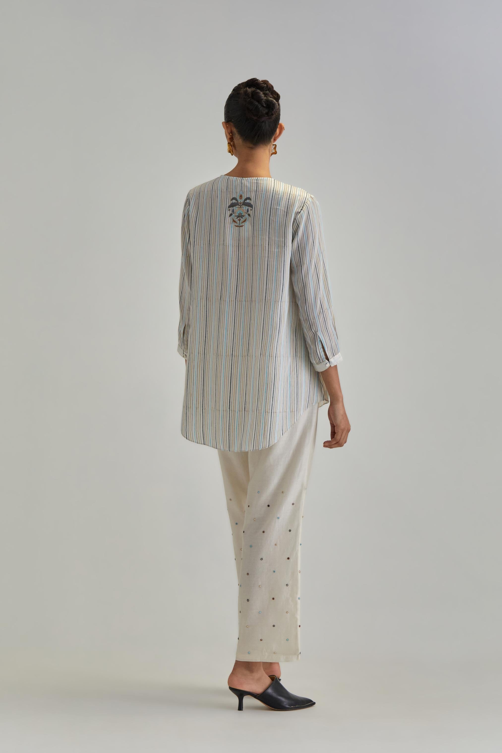 Off White short top with thin multi-coloured stripe hand block print and earthy coloured Aari thread embroidery, paired with Off White silk Chanderi straight pants with mirror work, highlighted with earthy coloured thread work.