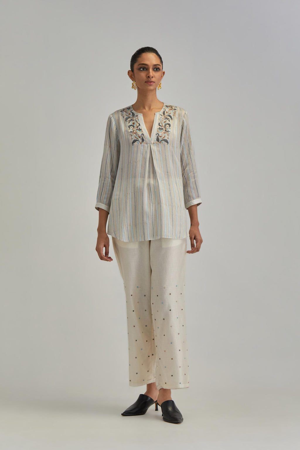Off White short top with thin multi-coloured stripe hand block print and earthy coloured Aari thread embroidery, paired with Off White silk Chanderi straight pants with mirror work, highlighted with earthy coloured thread work.