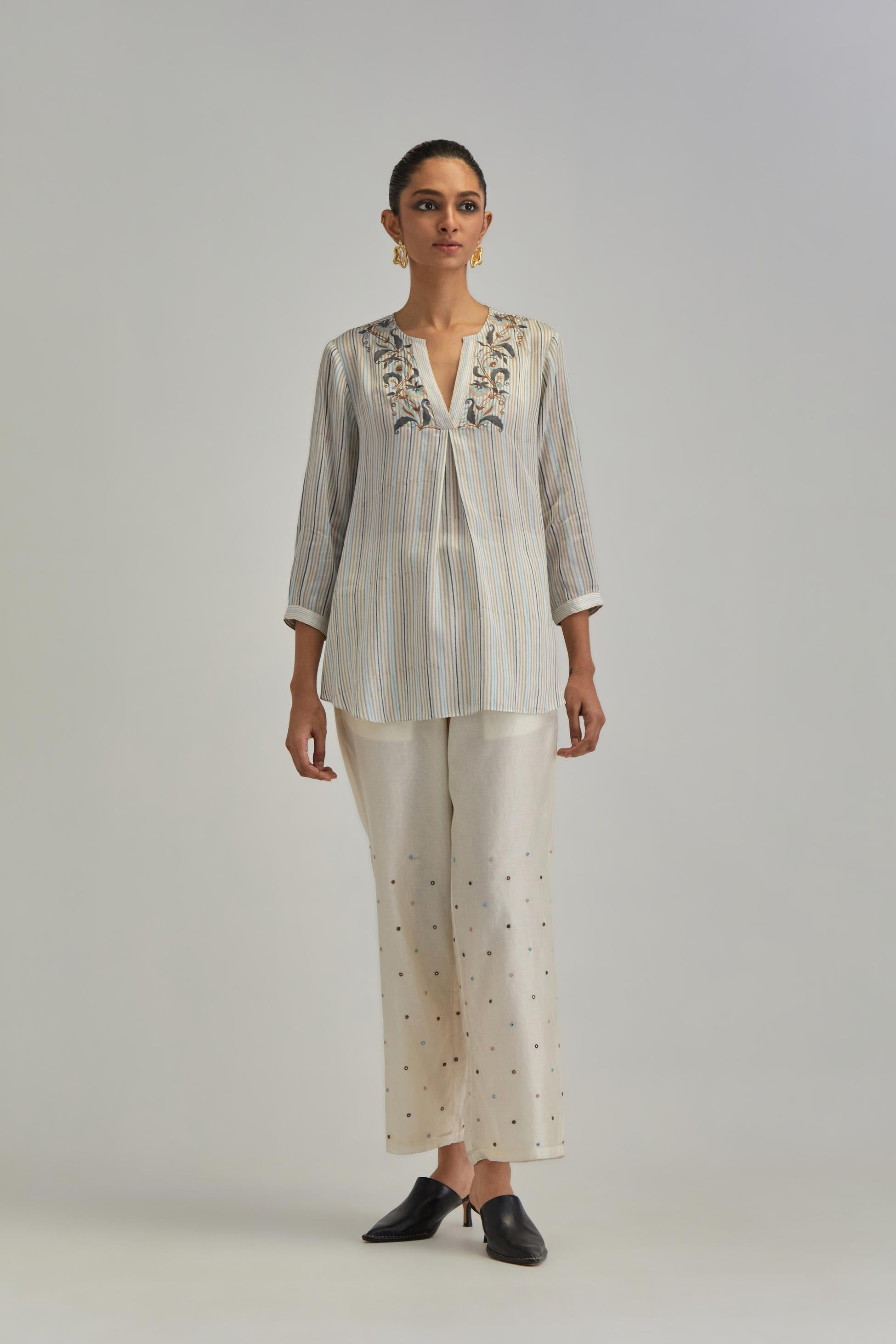 Off White short top with thin multi-coloured stripe hand block print and earthy coloured Aari thread embroidery, paired with Off White silk Chanderi straight pants with mirror work, highlighted with earthy coloured thread work.