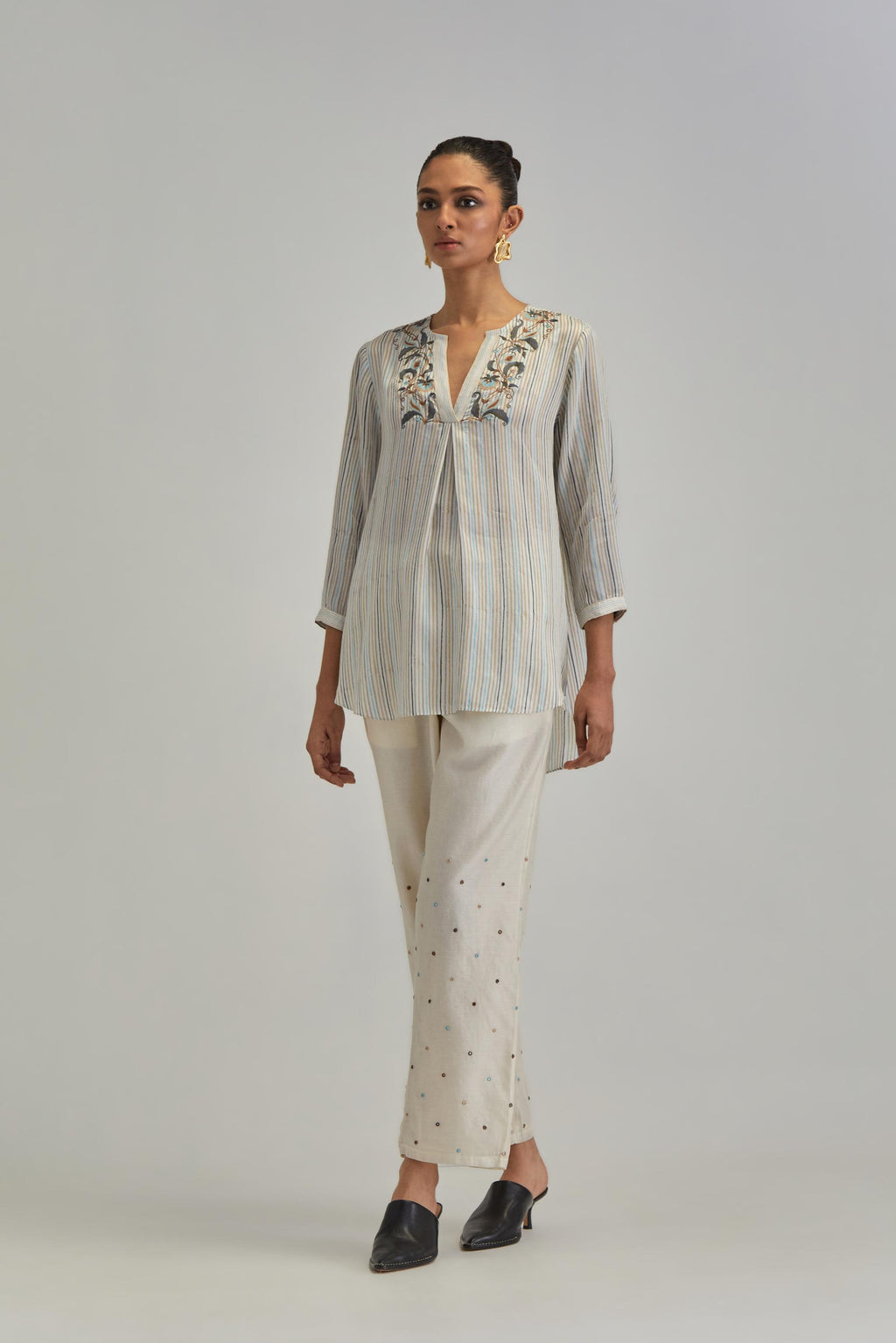 Off White short top with thin multi-coloured stripe hand block print and earthy coloured Aari thread embroidery, paired with Off White silk Chanderi straight pants with mirror work, highlighted with earthy coloured thread work.