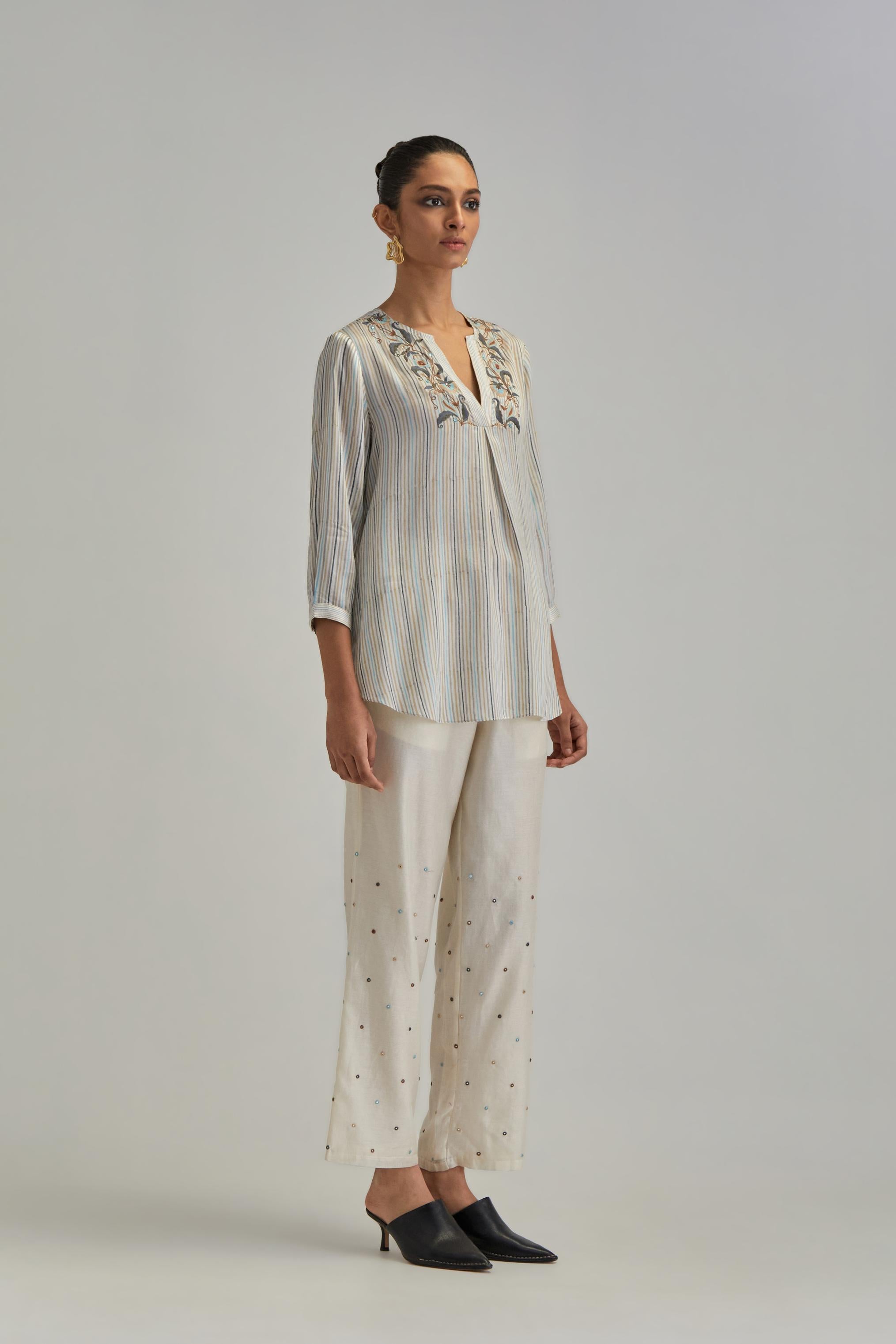 Off White short top with thin multi-coloured stripe hand block print and earthy coloured Aari thread embroidery, paired with Off White silk Chanderi straight pants with mirror work, highlighted with earthy coloured thread work.