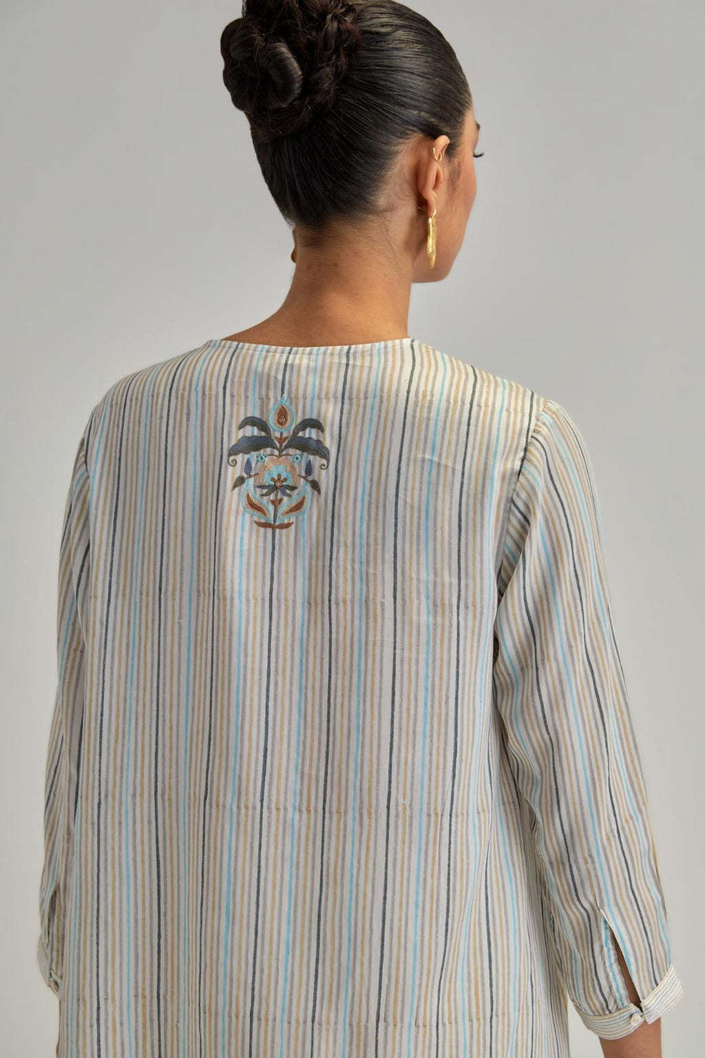 Off White short top with thin multi-coloured stripe hand block print and earthy coloured Aari thread embroidery, paired with Off White silk Chanderi straight pants with mirror work, highlighted with earthy coloured thread work.