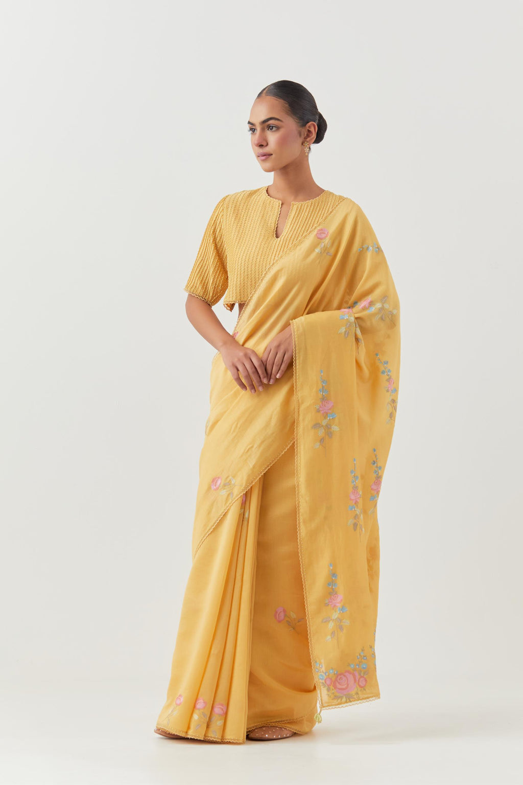 Yellow silk chanderi saree with all-over thread embroidered roses and scalloped organza with delicate bead detail at the edges, paired with yellow silk blouse with pin tucks, highlighted with bead work.