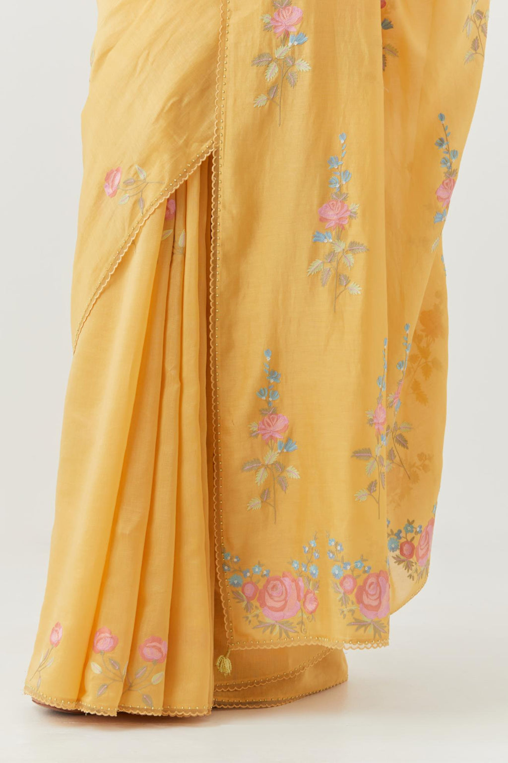 Yellow silk chanderi saree with all-over thread embroidered roses and scalloped organza with delicate bead detail at the edges, paired with yellow silk blouse with pin tucks, highlighted with bead work.