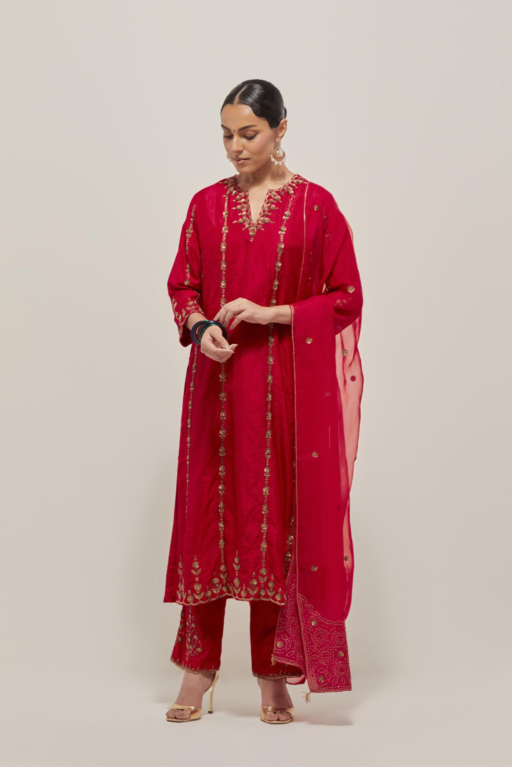 Red silk straight kurta set with round neck and slit in front. It has hand embroidered zardozi and sequins chhari stripes, all-over and heavier butas at hem, highlighted with beads.