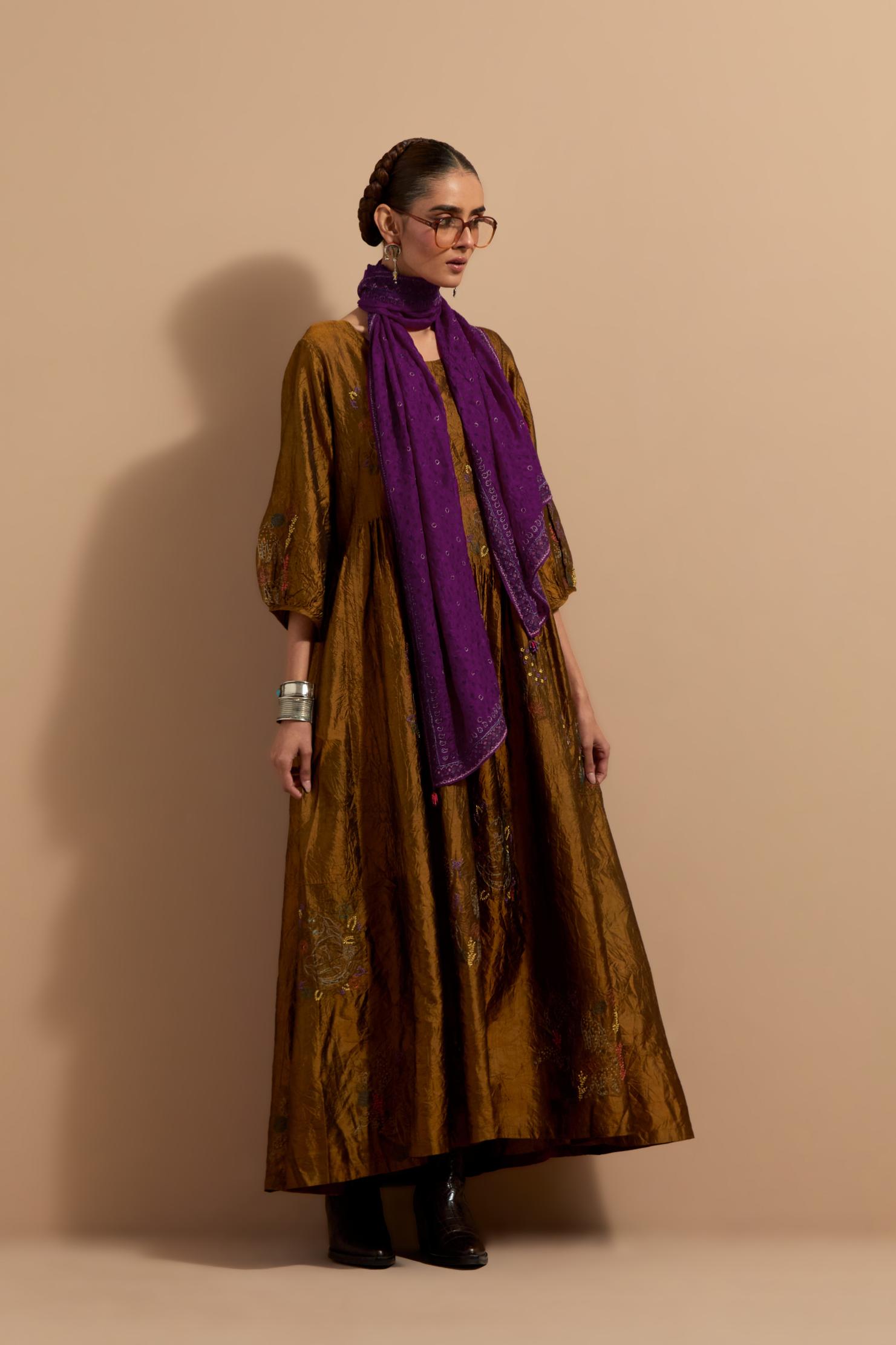 Olive crushed silk hand block printed long dress, highlighted with multi colored thread embroidery, paired with Purple hand crushed block printed silk stole with quilted embroidery and beaded tassels.
