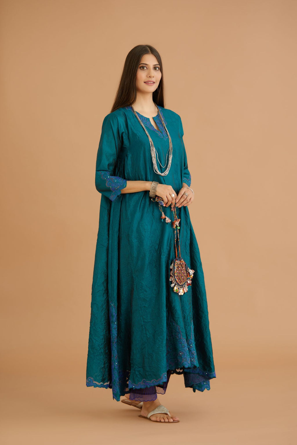 Teal green hand crushed silk kurta with cutwork embroidered asymmetric hem, highlighted with hand attached mirrors, paired with blue hand crushed silk pants with hand block print fine stripes and organza fabric and embroidery detail at bottom hem.