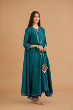 Teal green hand crushed silk kurta with cutwork embroidered asymmetric hem, highlighted with hand attached mirrors, paired with blue hand crushed silk pants with hand block print fine stripes and organza fabric and embroidery detail at bottom hem.