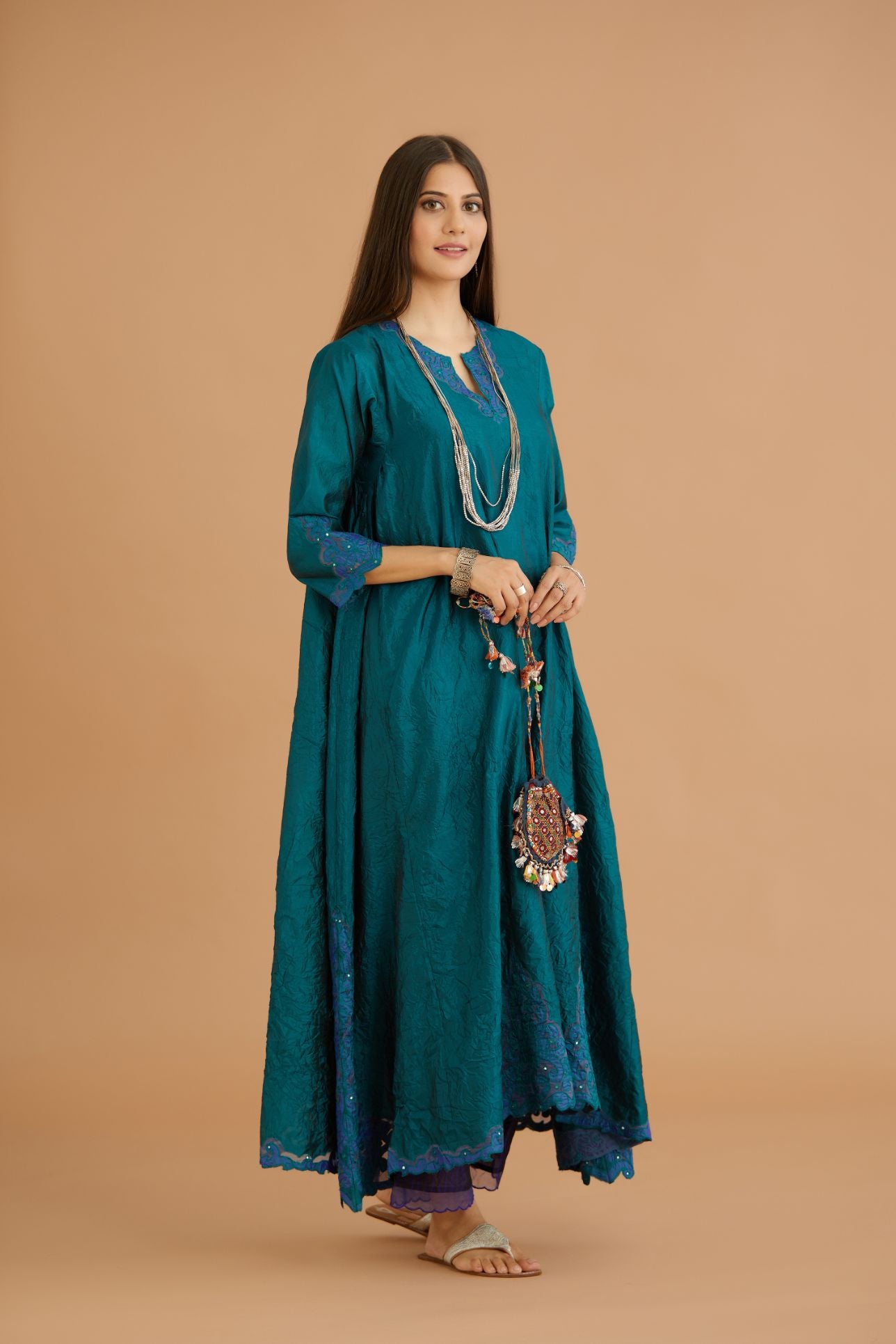 Teal green hand crushed silk kurta with cutwork embroidered asymmetric hem, highlighted with hand attached mirrors, paired with blue hand crushed silk pants with hand block print fine stripes and organza fabric and embroidery detail at bottom hem.