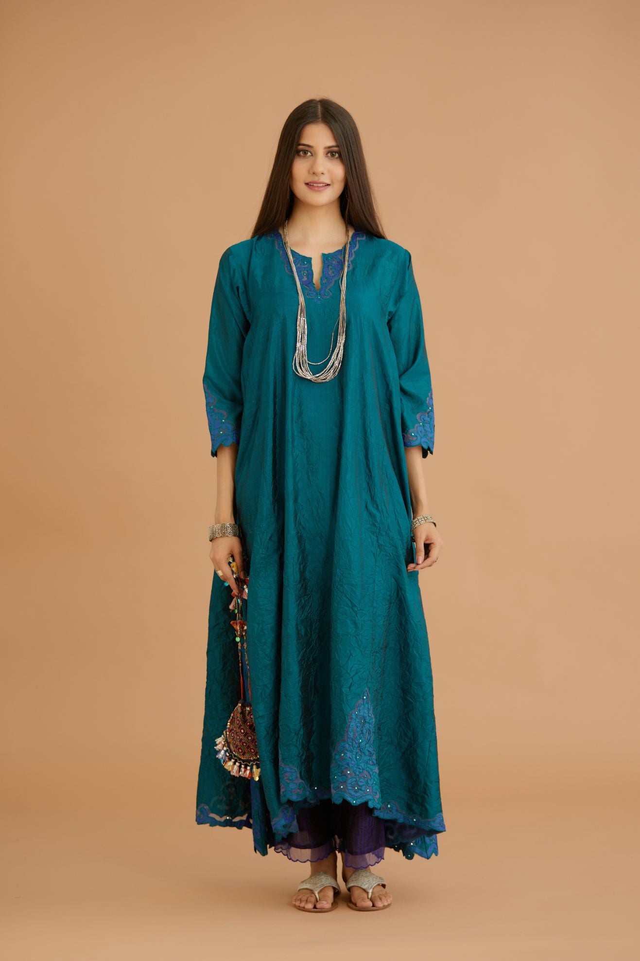 Teal green hand crushed silk kurta with cutwork embroidered asymmetric hem, highlighted with hand attached mirrors, paired with blue hand crushed silk pants with hand block print fine stripes and organza fabric and embroidery detail at bottom hem.