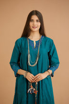 Teal green hand crushed silk kurta with cutwork embroidered asymmetric hem, highlighted with hand attached mirrors, paired with blue hand crushed silk pants with hand block print fine stripes and organza fabric and embroidery detail at bottom hem.
