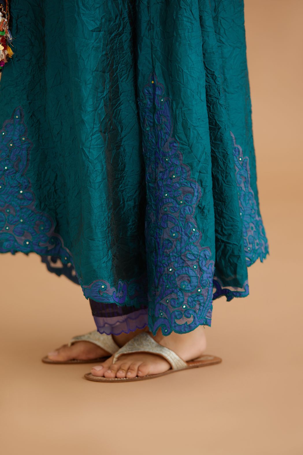 Teal green hand crushed silk kurta with cutwork embroidered asymmetric hem, highlighted with hand attached mirrors, paired with blue hand crushed silk pants with hand block print fine stripes and organza fabric and embroidery detail at bottom hem.
