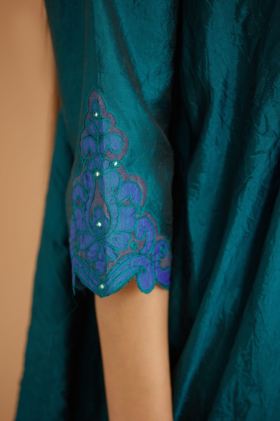 Teal green hand crushed silk kurta with cutwork embroidered asymmetric hem, highlighted with hand attached mirrors, paired with blue hand crushed silk pants with hand block print fine stripes and organza fabric and embroidery detail at bottom hem.