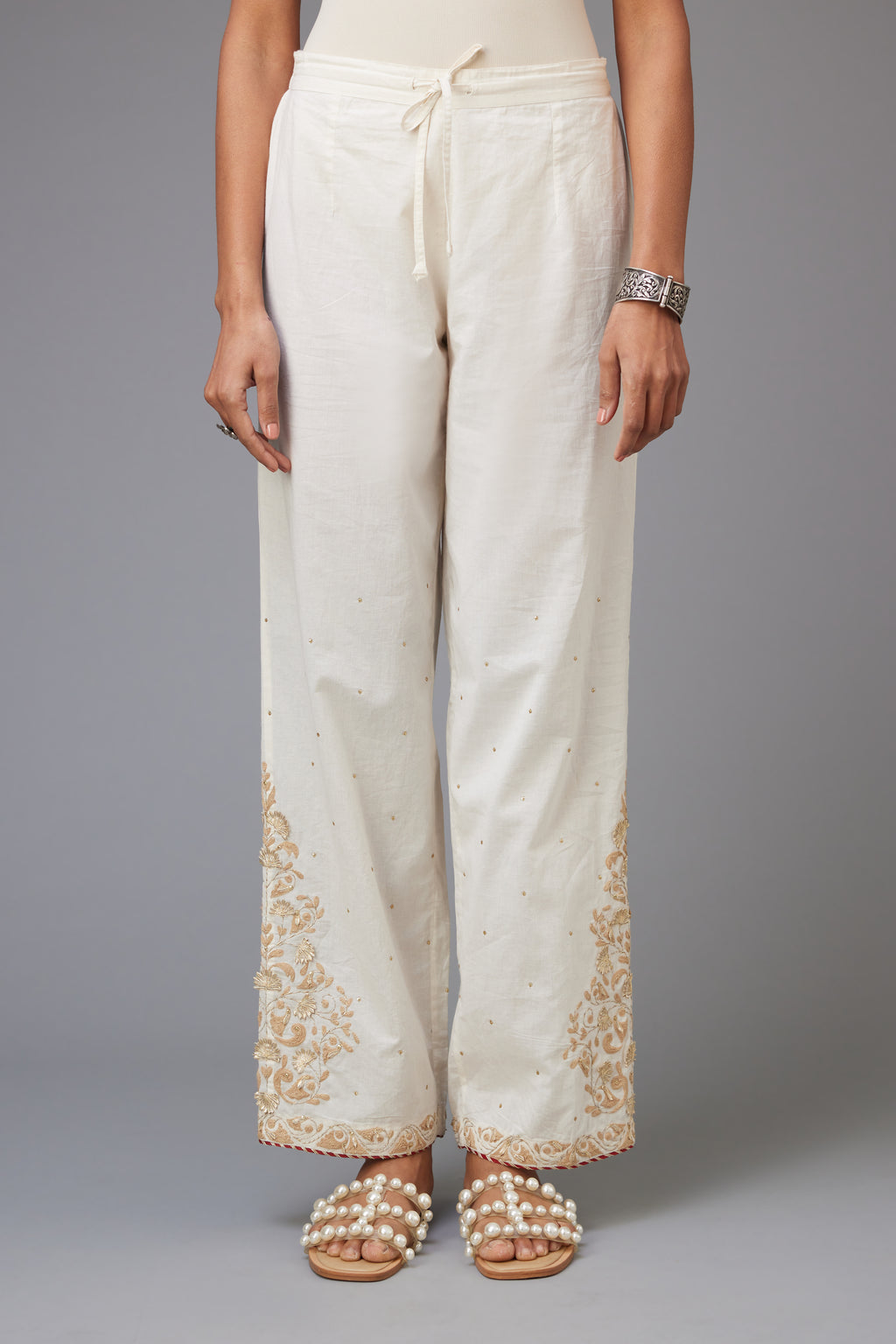Off-white cotton straight pants, hem is detailed with dori and gota embroidered boota at sides.