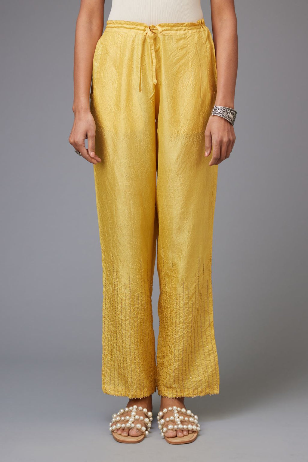 Yellow hand crushed silk straight pants with golden sequin lines from calf to hem, highlighted with gota lace at edges.