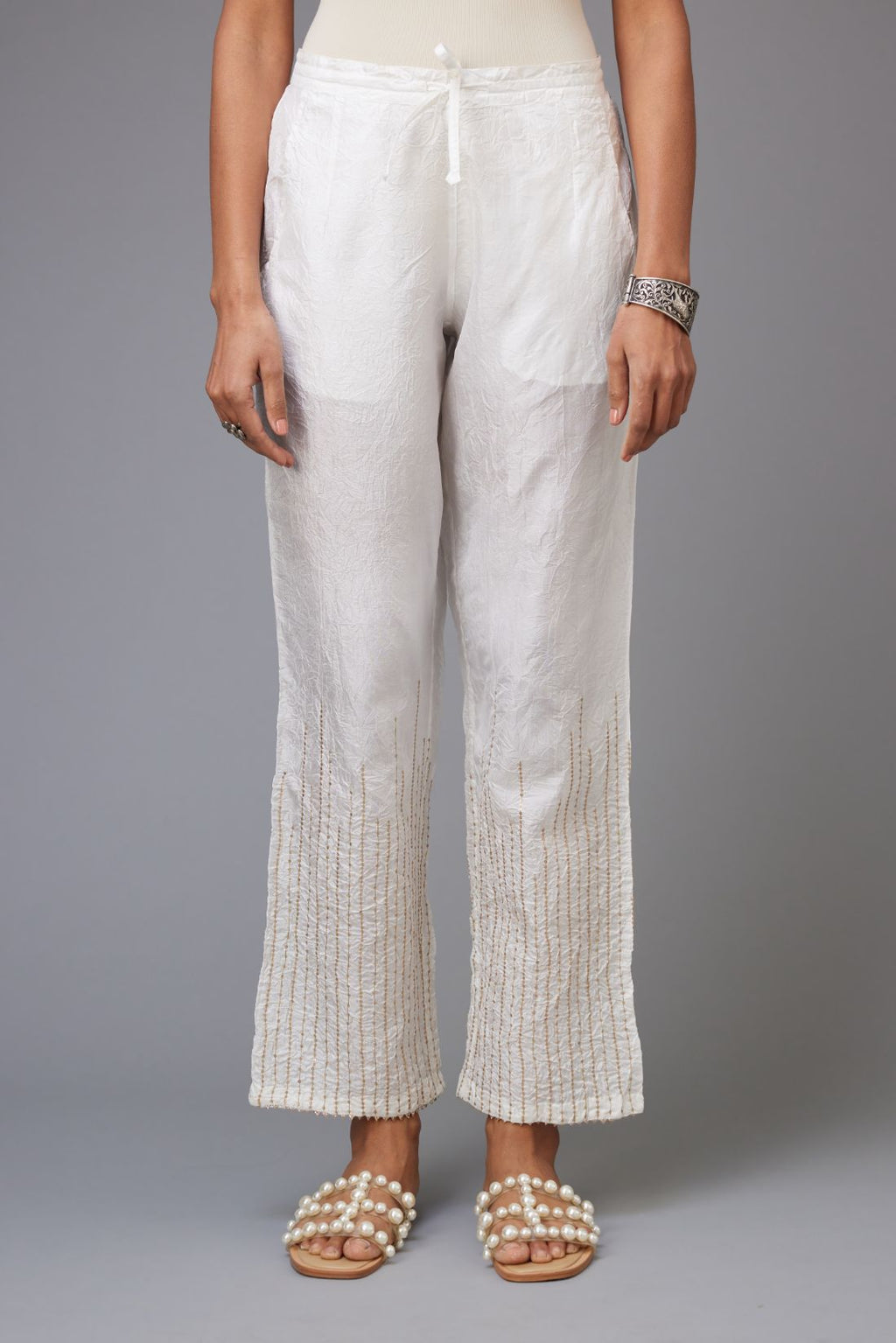 White hand crushed silk straight pants with golden sequin lines from calf to hem, highlighted with gota lace at edges.