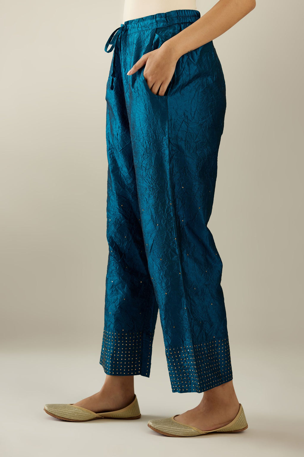 Dark teal hand crushed silk straight pants detailed with gold sequins at hem and a single sequin buti is sprayed all over the pants and side pockets