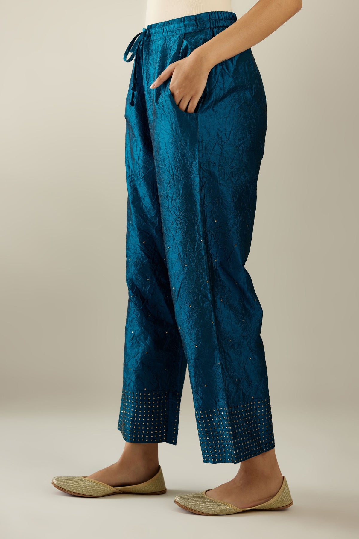 Dark teal hand crushed silk straight pants detailed with gold sequins at hem and a single sequin buti is sprayed all over the pants and side pockets