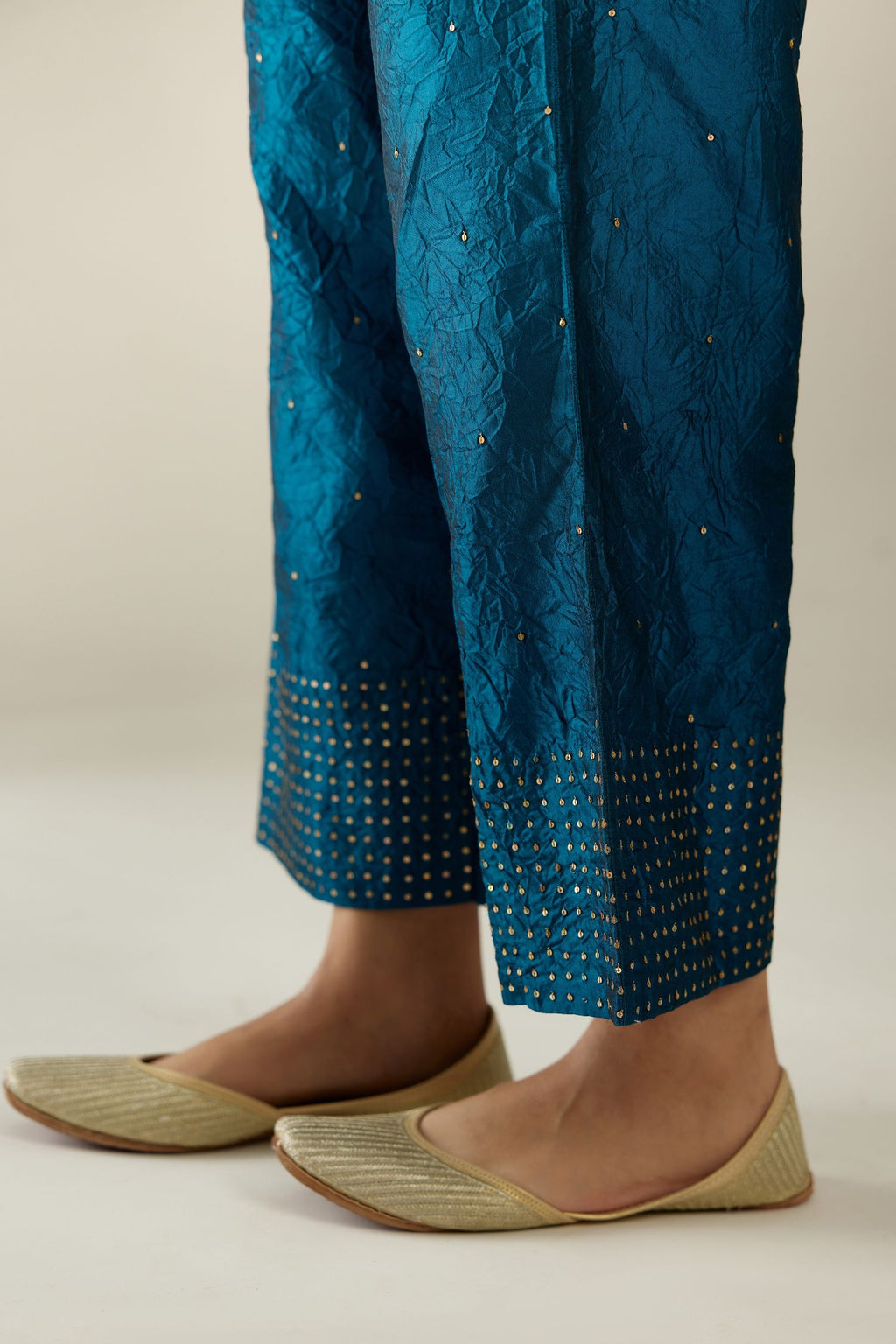 Dark teal hand crushed silk straight pants detailed with gold sequins at hem and a single sequin buti is sprayed all over the pants and side pockets