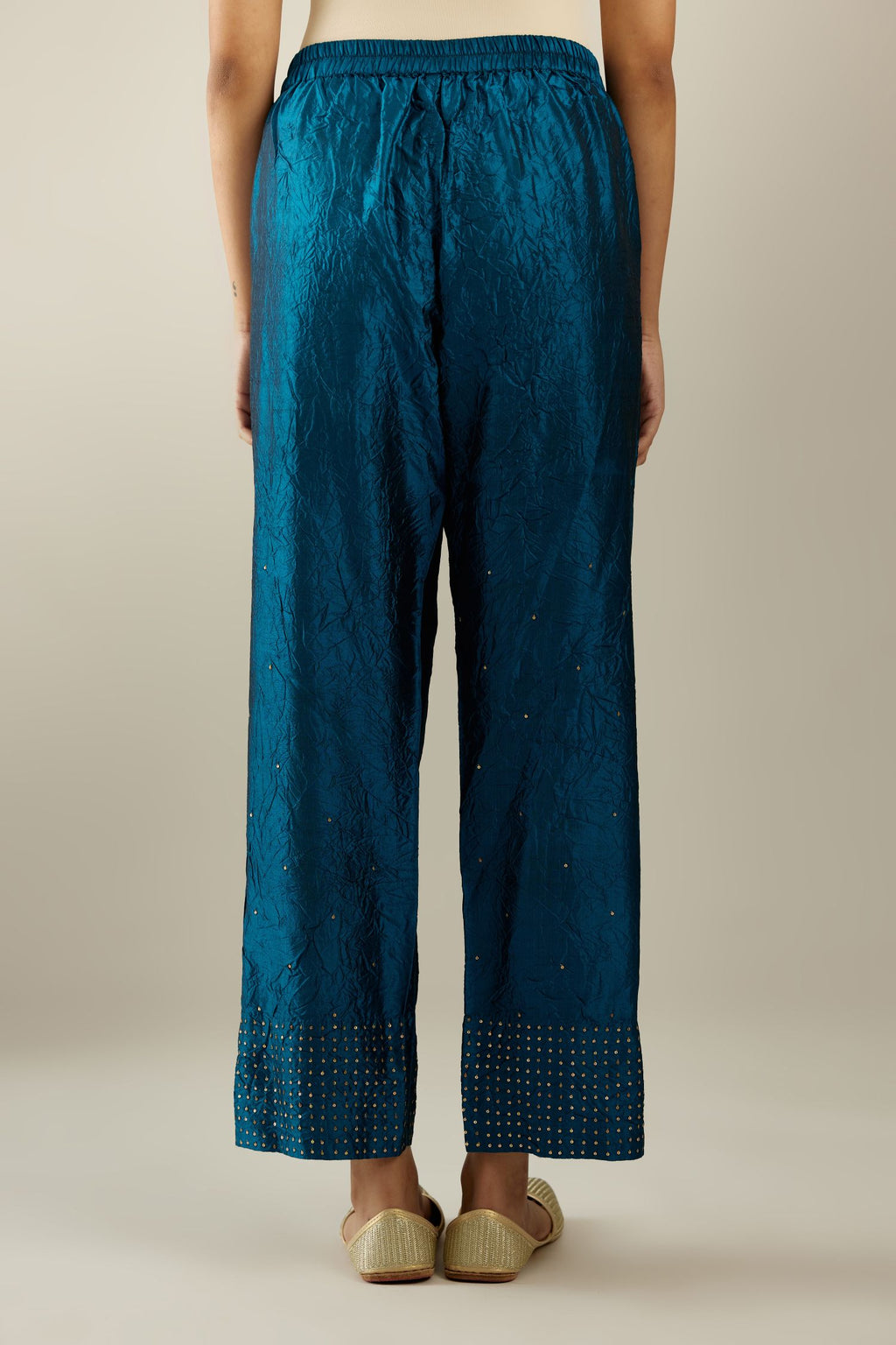 Dark teal hand crushed silk straight pants detailed with gold sequins at hem and a single sequin buti is sprayed all over the pants and side pockets