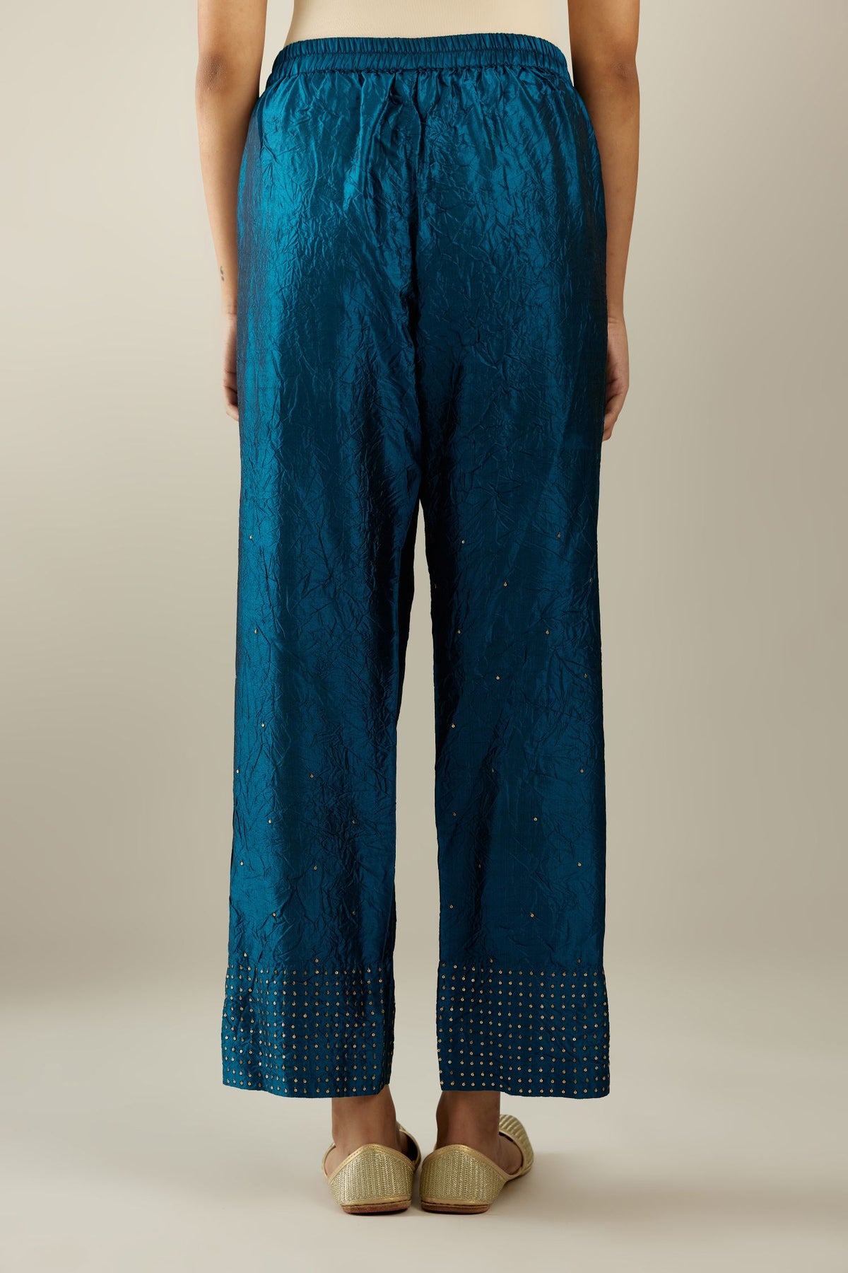 Dark teal hand crushed silk straight pants detailed with gold sequins at hem and a single sequin buti is sprayed all over the pants and side pockets