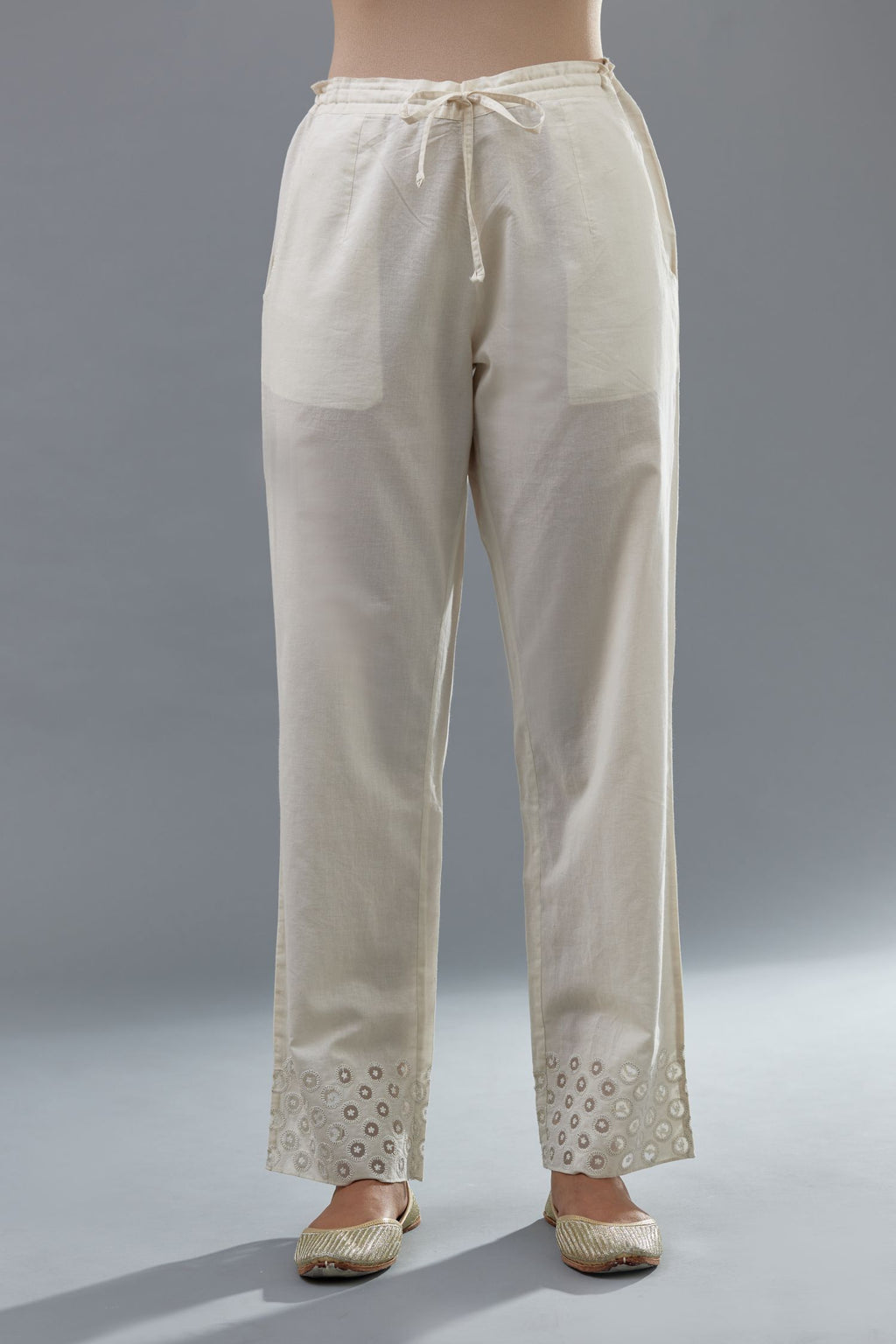 Off white cotton straight pants with appliqué and dori embroidery work at bottom hem.