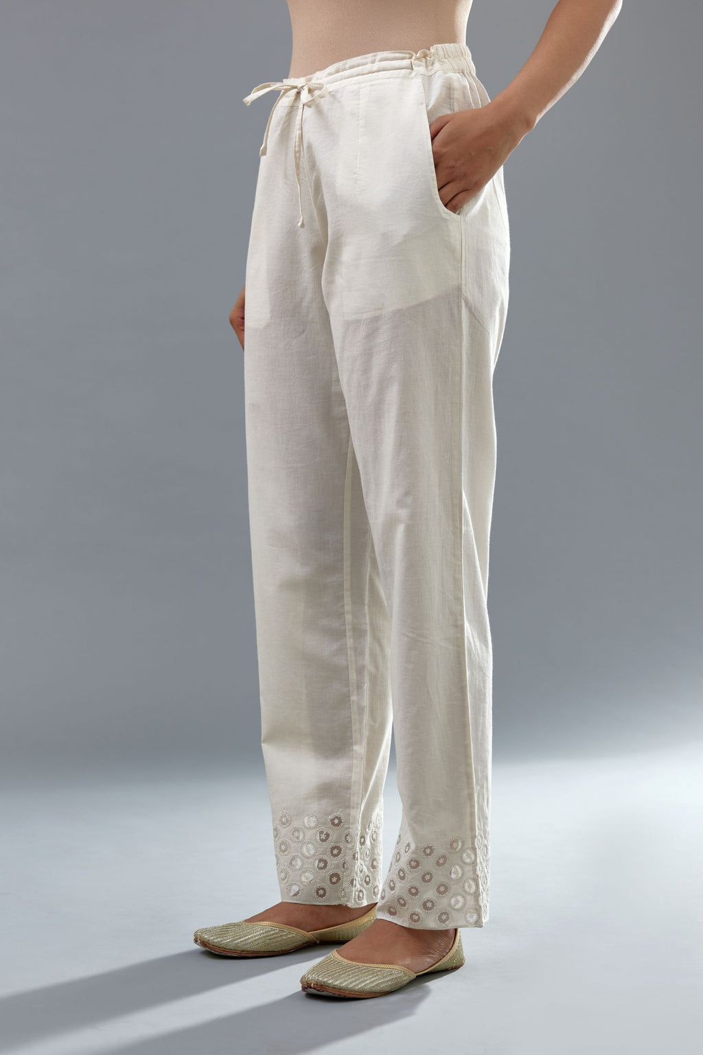 Off white cotton straight pants with appliqué and dori embroidery work at bottom hem.