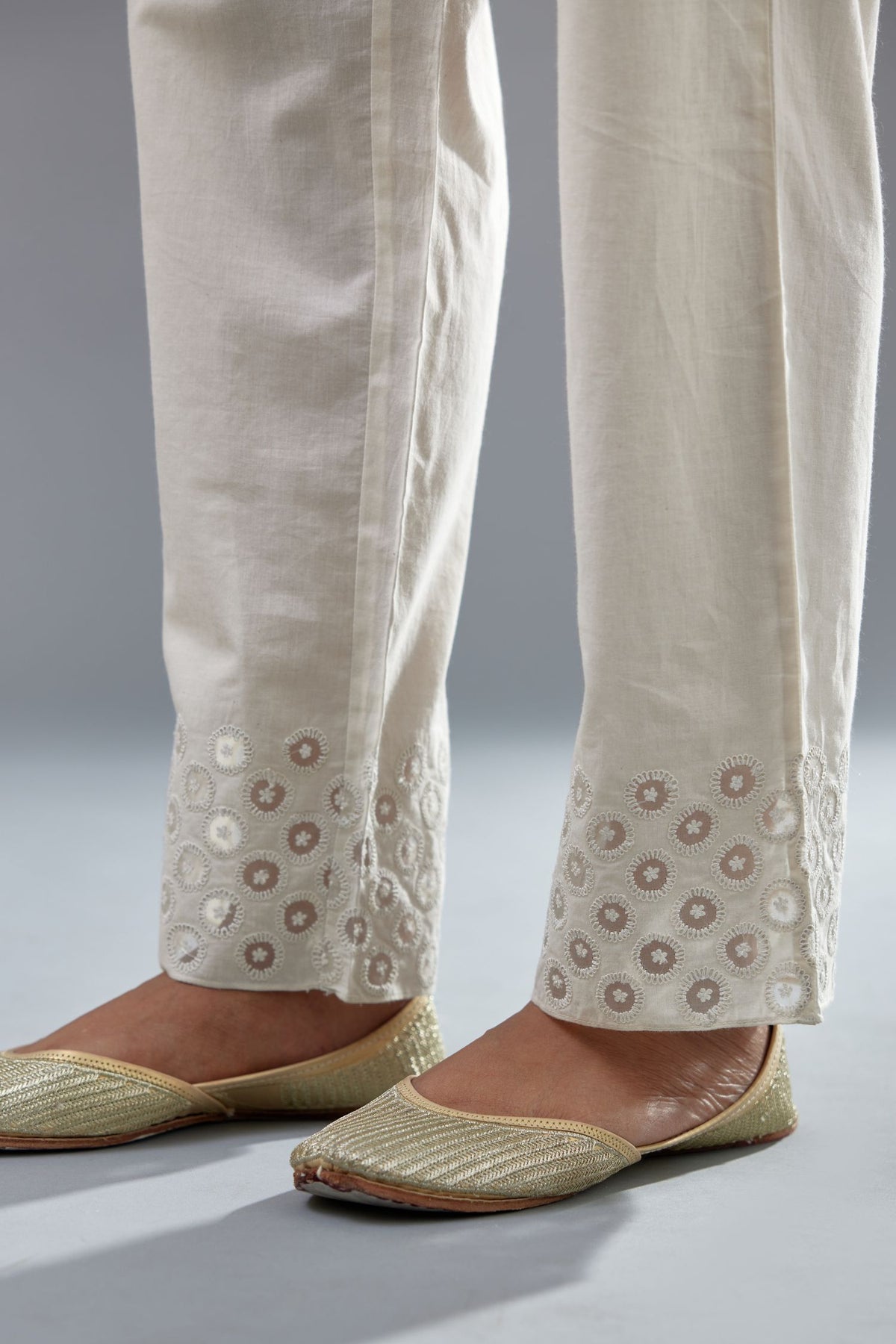 Off white cotton straight pants with appliqué and dori embroidery work at bottom hem.