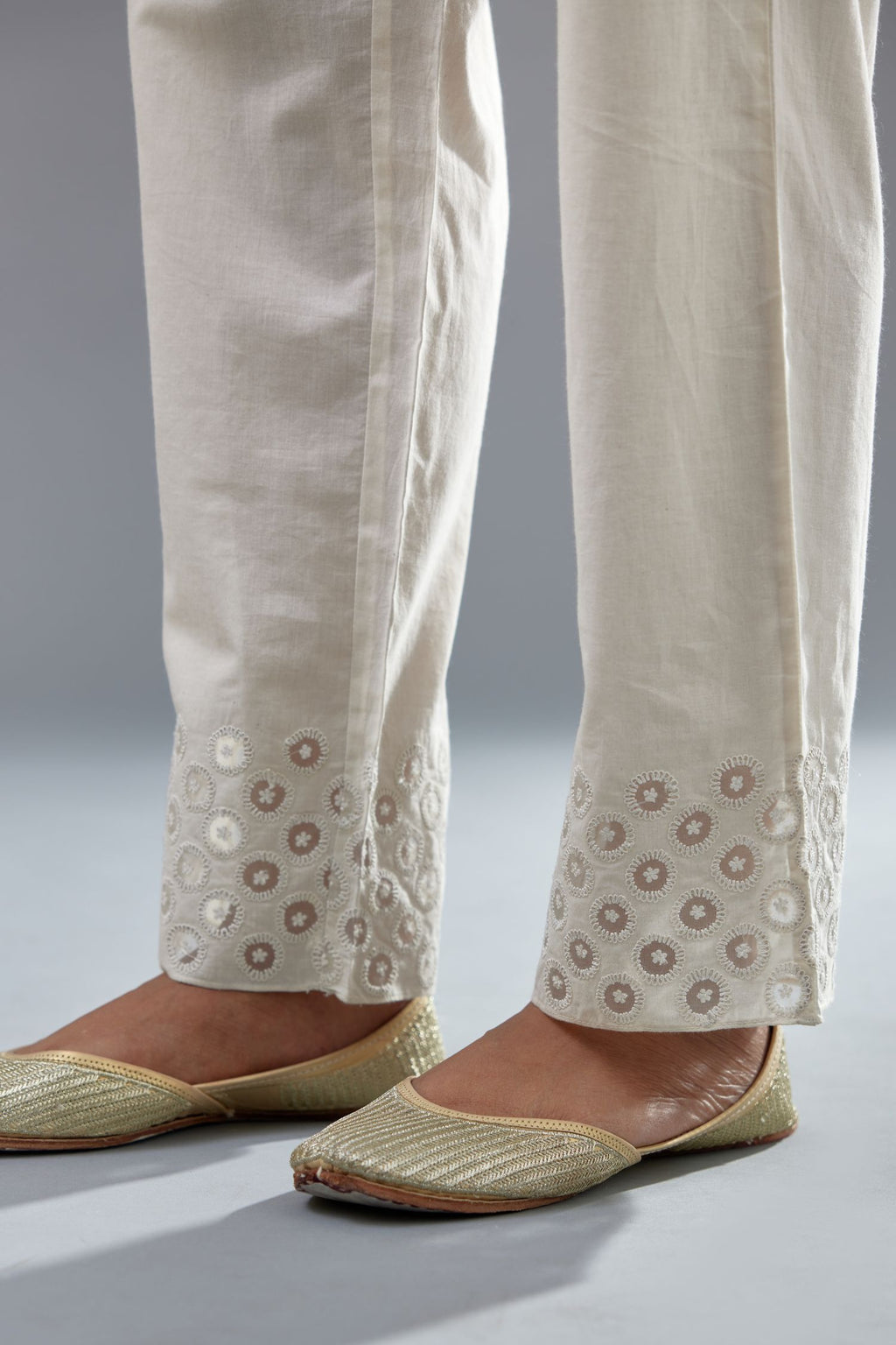 Off white cotton straight pants with appliqué and dori embroidery work at bottom hem.