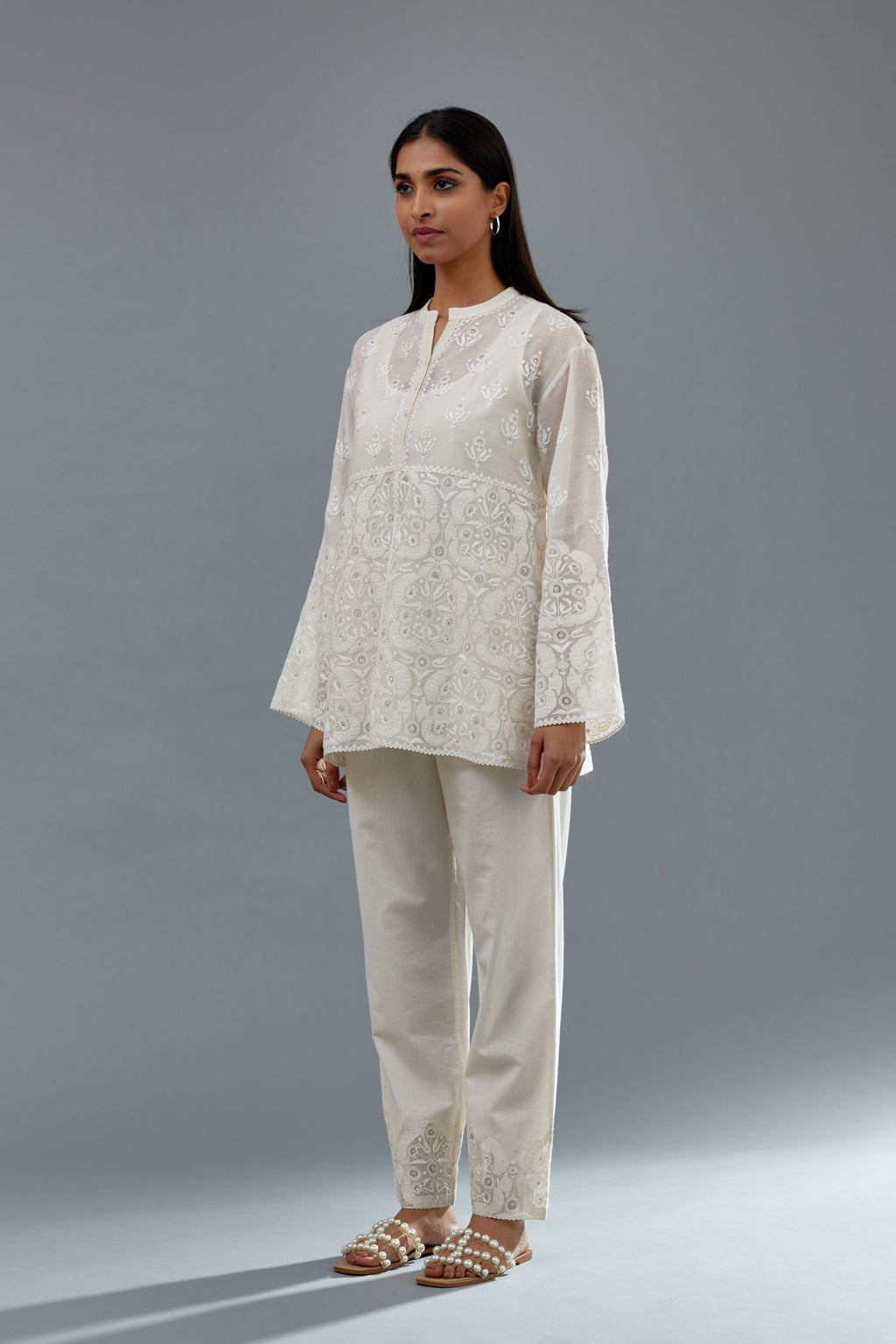 Off white cotton chanderi short top with heavy appliqué, highlighted with sequins, paired with off white cotton straight pants with appliqué and hand attached sequins detailing at bottom hem.