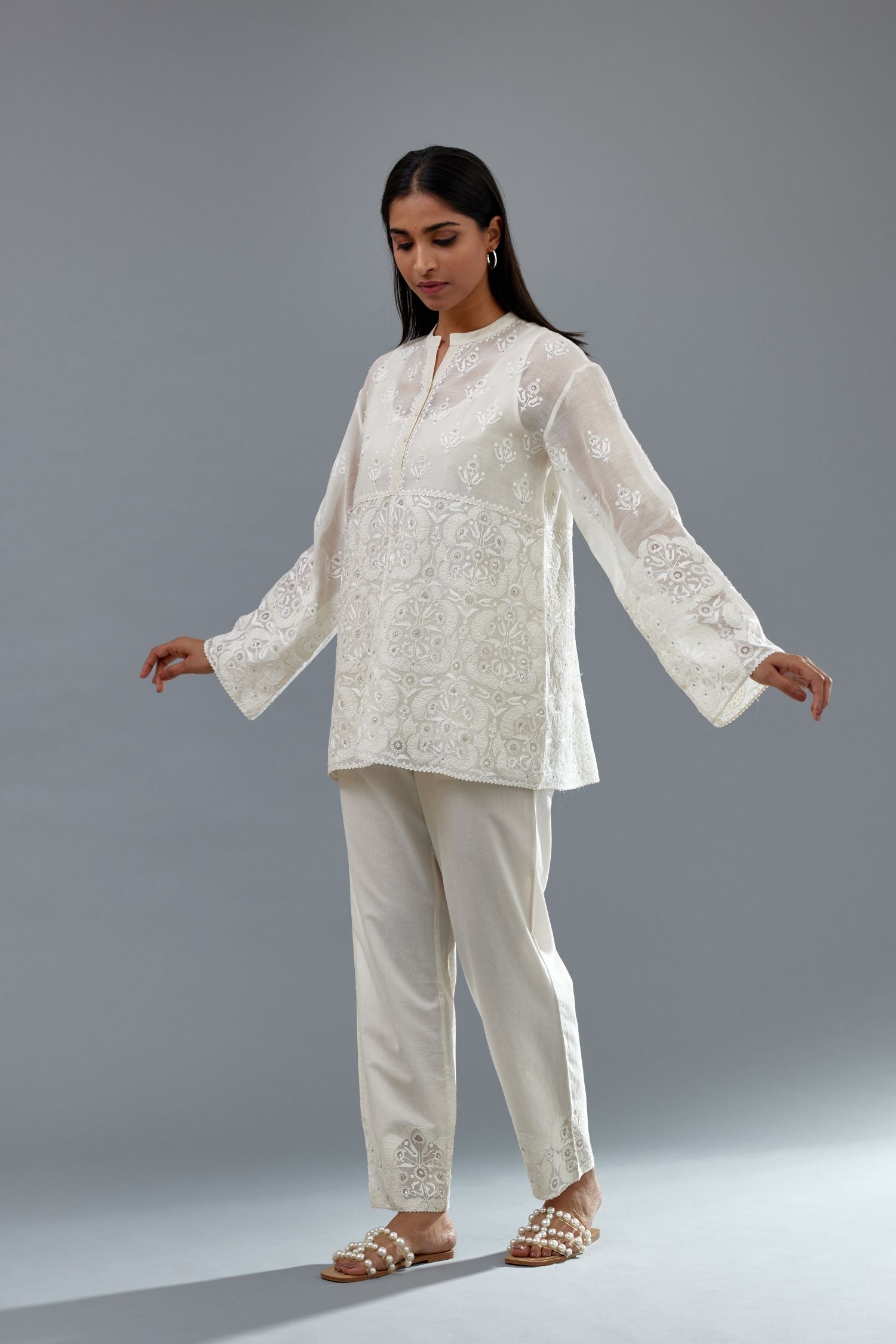 Off white cotton chanderi short top with heavy appliqué, highlighted with sequins, paired with off white cotton straight pants with appliqué and hand attached sequins detailing at bottom hem.