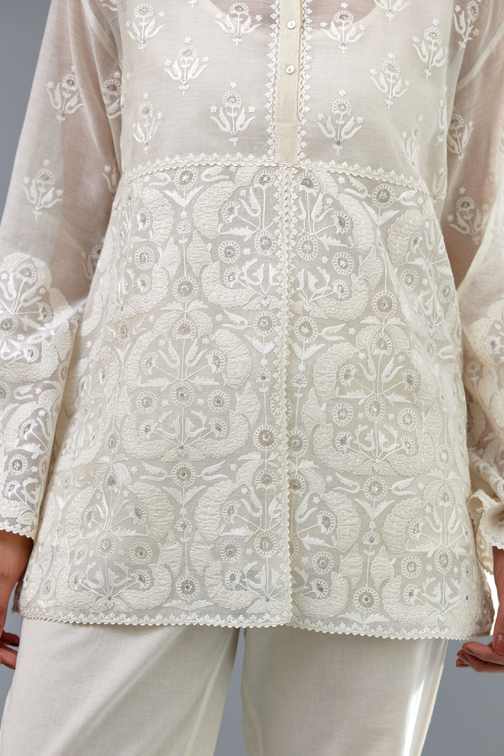 Off white cotton chanderi short top with heavy appliqué, highlighted with sequins, paired with off white cotton straight pants with appliqué and hand attached sequins detailing at bottom hem.