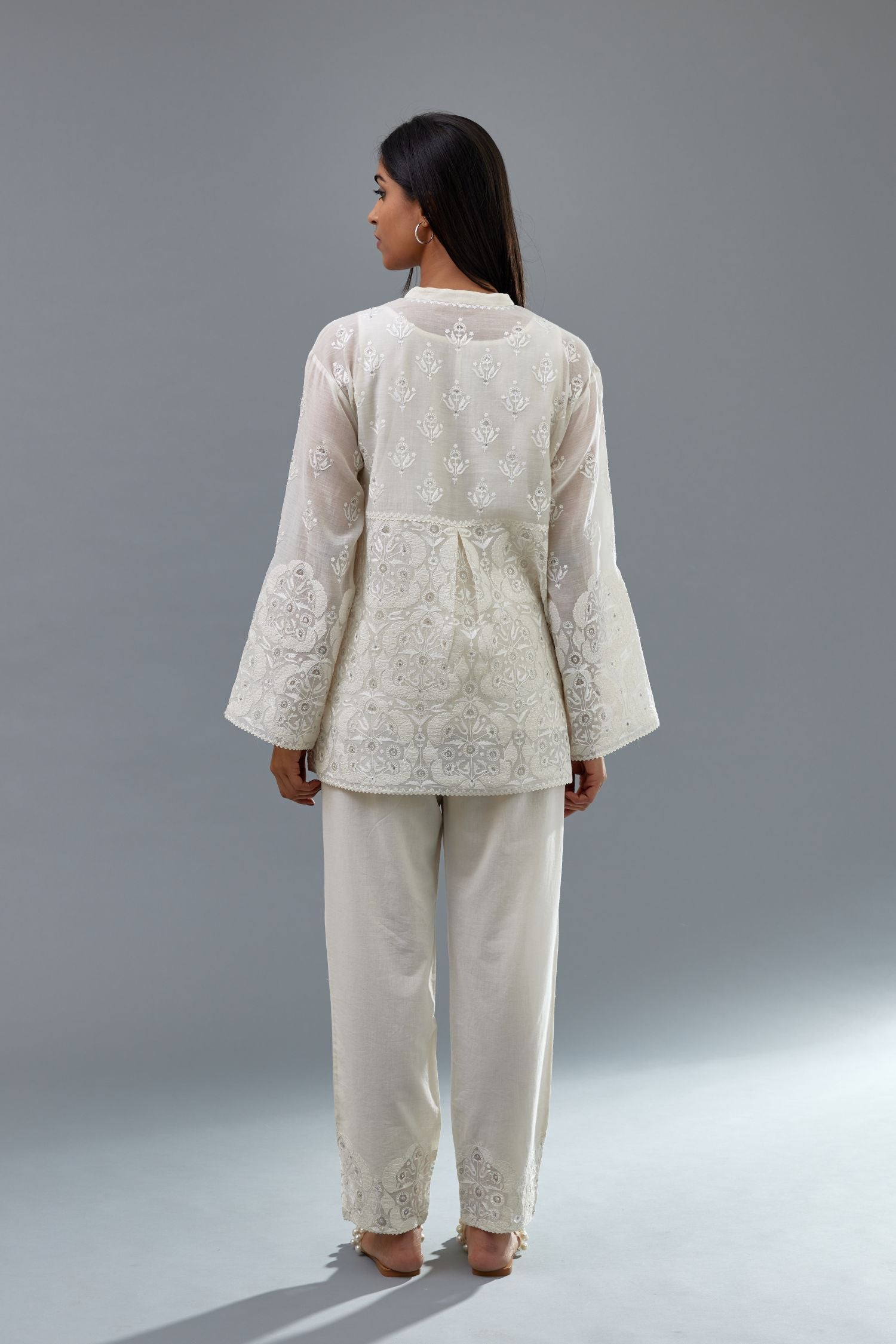 Off white cotton chanderi short top with heavy appliqué, highlighted with sequins, paired with off white cotton straight pants with appliqué and hand attached sequins detailing at bottom hem.
