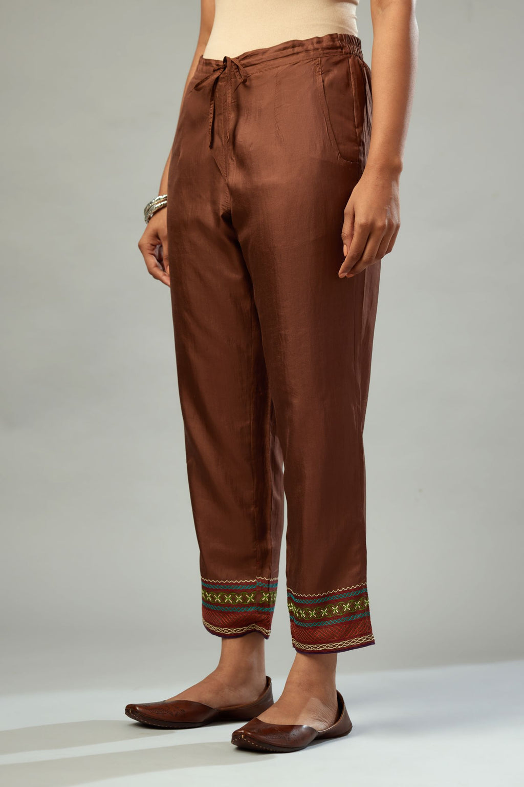 Brown silk straight pants detailed with quilted multi colored embroidery at bottom.