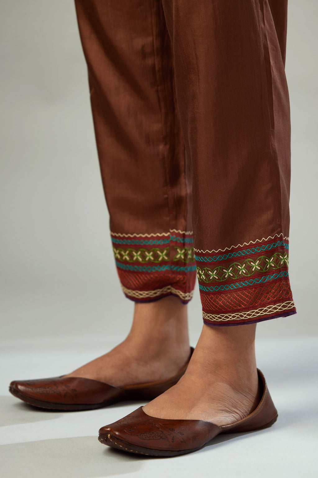 Brown silk straight pants detailed with quilted multi colored embroidery at bottom.